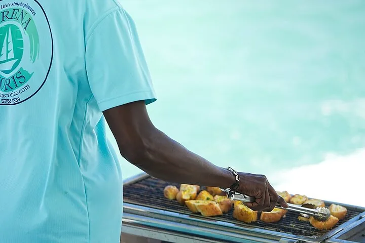 Membro dell'equipaggio che griglia cibo su un barbecue a bordo di una barca in acque tropicali.