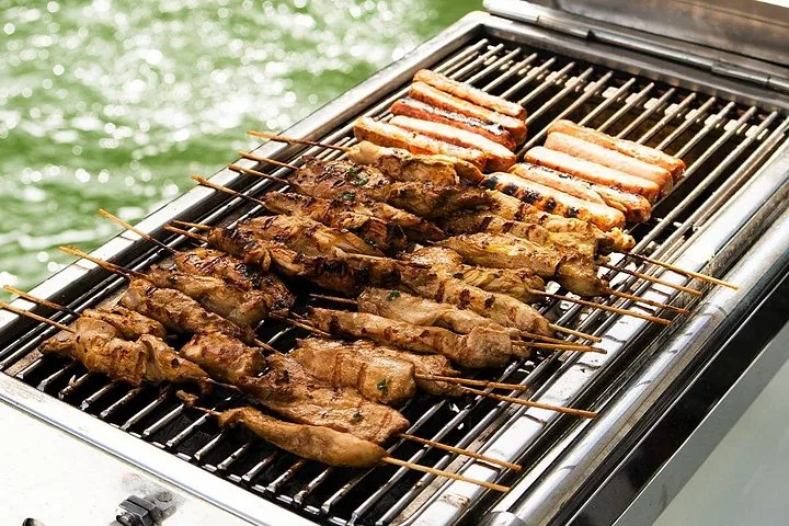 Spiedini di pollo e salsicce che cuociono sulla griglia barbecue di una barca sull'acqua.
