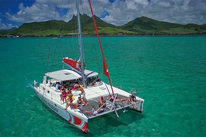 Des personnes se détendent sur un grand catamaran naviguant dans des eaux tropicales claires et peu profondes.