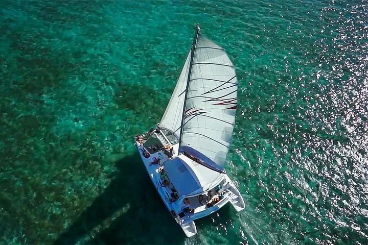 Vue aérienne d'un catamaran naviguant sur une eau turquoise claire et peu profonde.